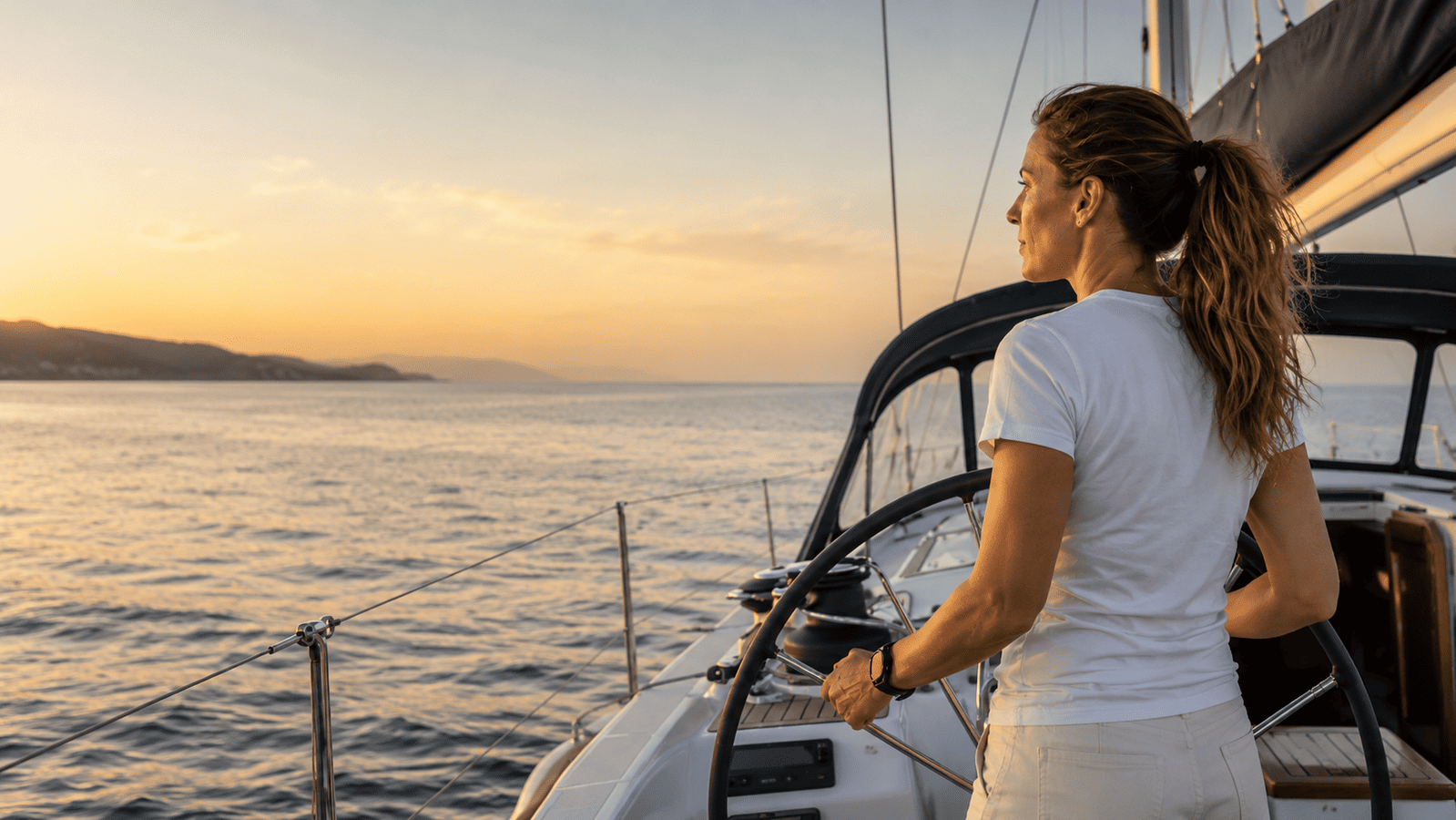 Seglerin auf Segelyacht am Ruder vor der Küste auf dem Meer bei Sonnenuntergang